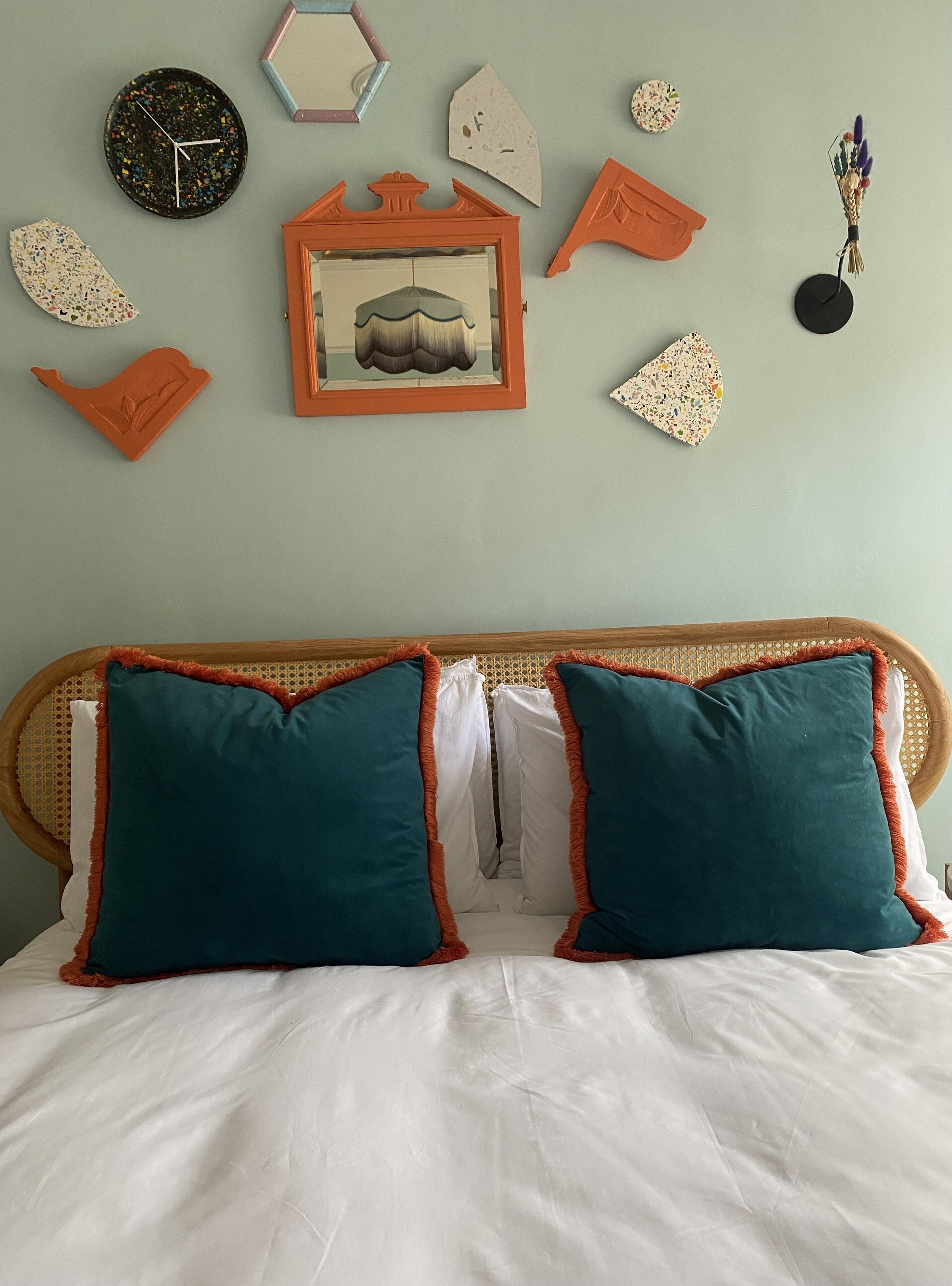 Un lit avec des oreillers de couleur turquoise et une tête de lit en bois, une horloge et divers éléments de décoration murale, notamment un tableau encadré et des formes géométriques.
