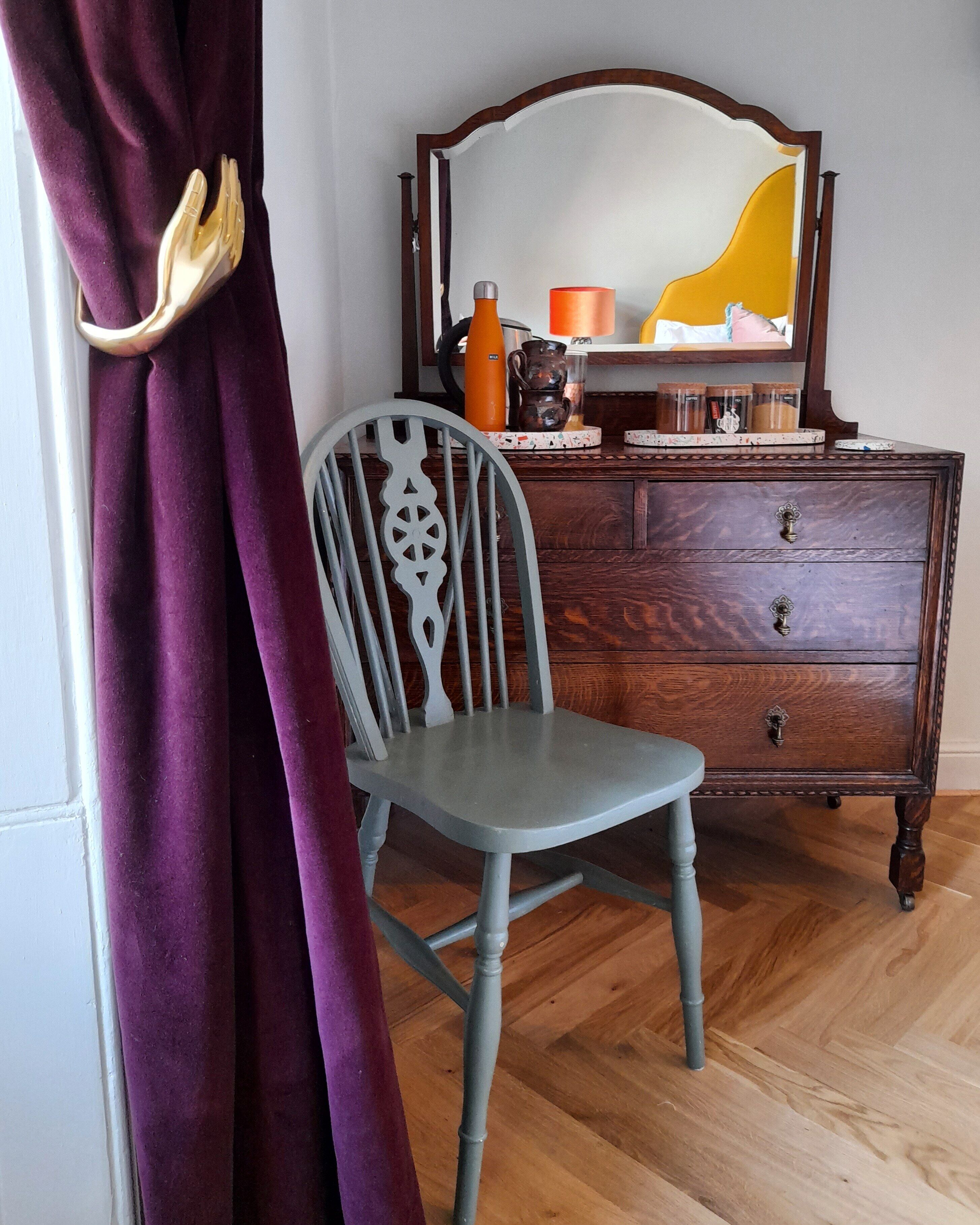 A room with a wooden dresser, a chair, and a mirror.