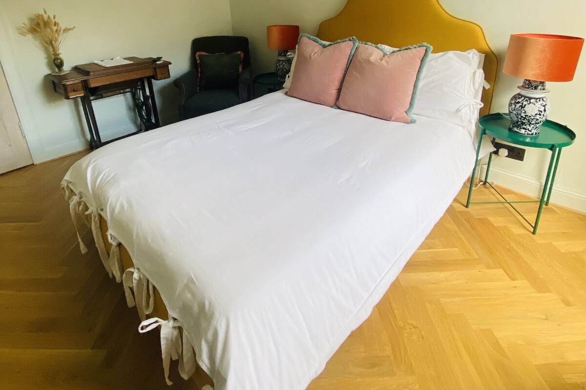 A bedroom with a large bed, a desk, a chair, a lamp, and a painting on the wall.