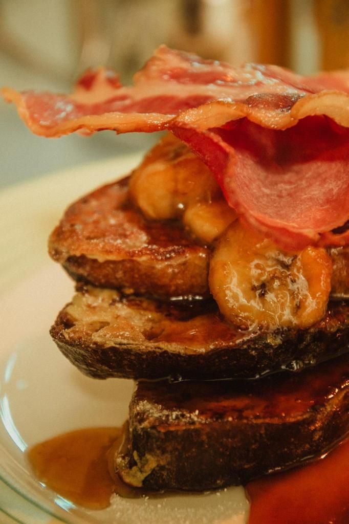 Ein Stapel Pfannkuchen mit Bananen und Speck, serviert auf einem Teller mit Ahornsirup.