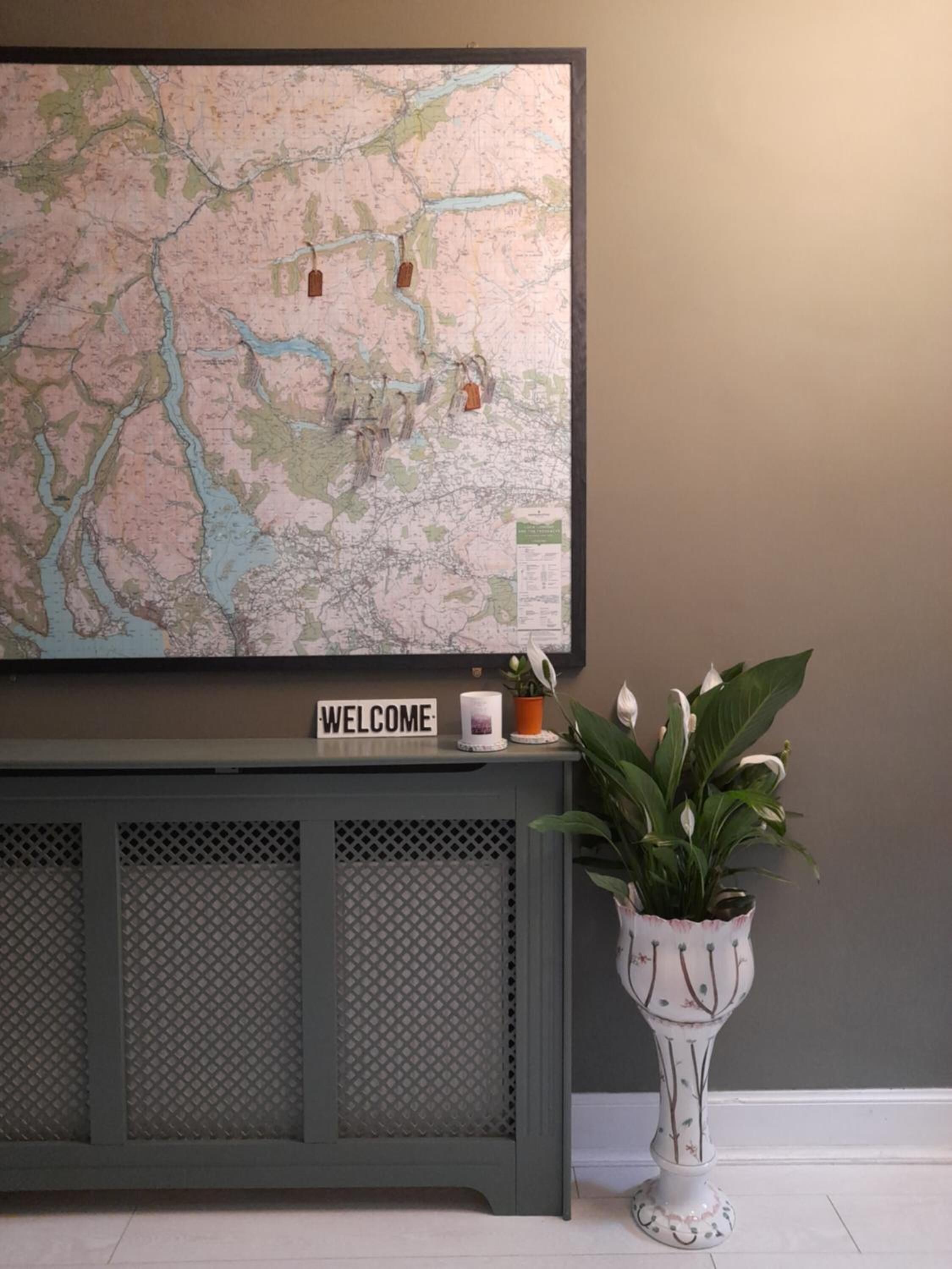 Un mapa en la pared, un cartel de bienvenida, una planta en maceta y una consola gris.