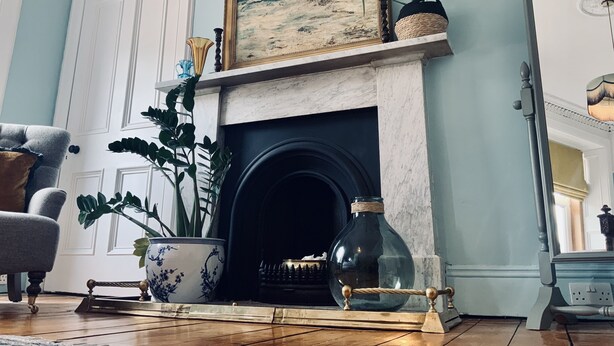 A room with a fireplace, a framed painting, a potted plant, a vase, and a chair. - Ben A'an House (Callander)