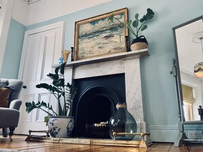 A room with a fireplace, a framed painting, a potted plant, a vase, and a chair. - Ben A'an House (Callander)