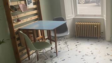 Un coin repas avec une table et des chaises en bois, un radiateur et une fenêtre donnant sur la rue.