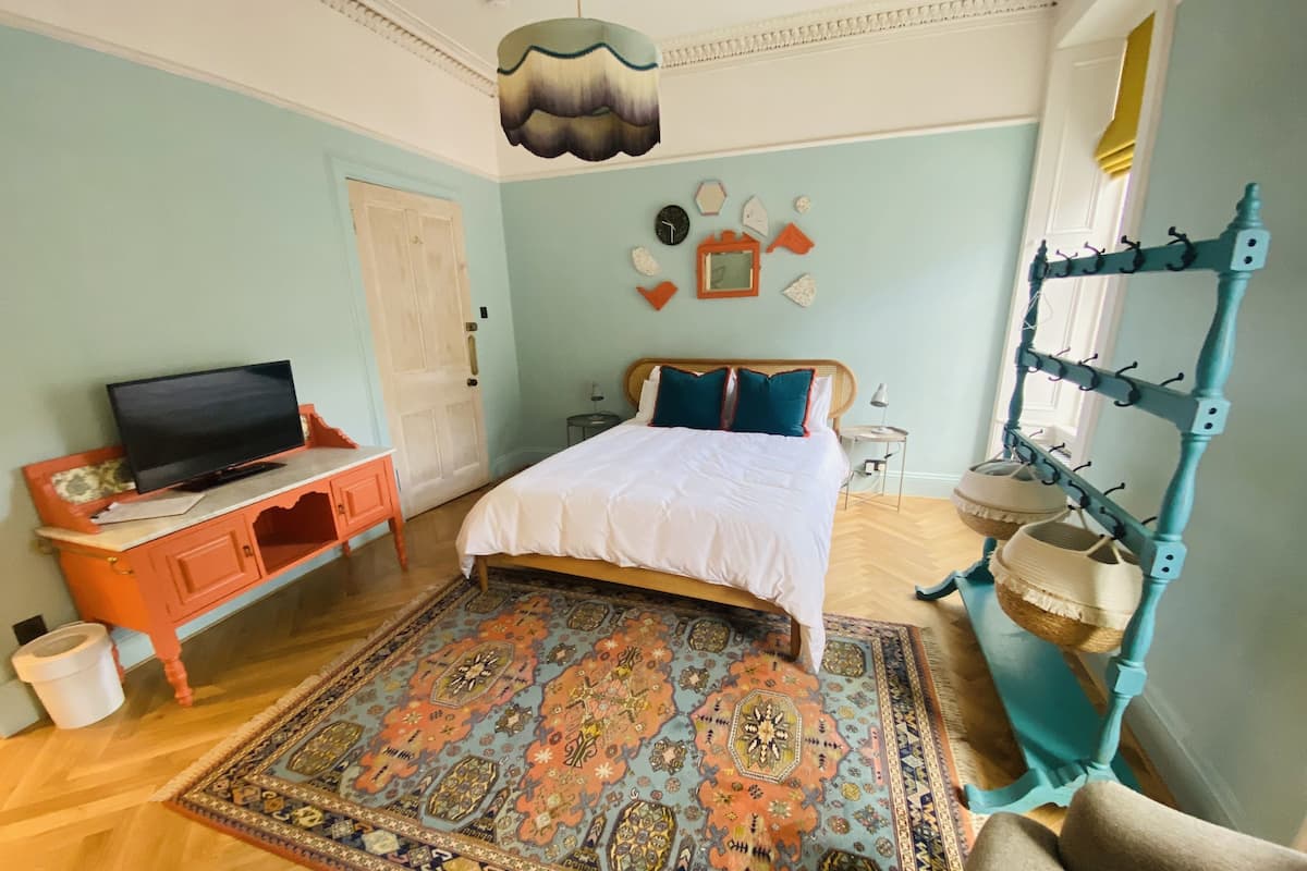 A bedroom with a bed, a television on a stand, a decorative rug, and a wall-mounted rack with baskets.