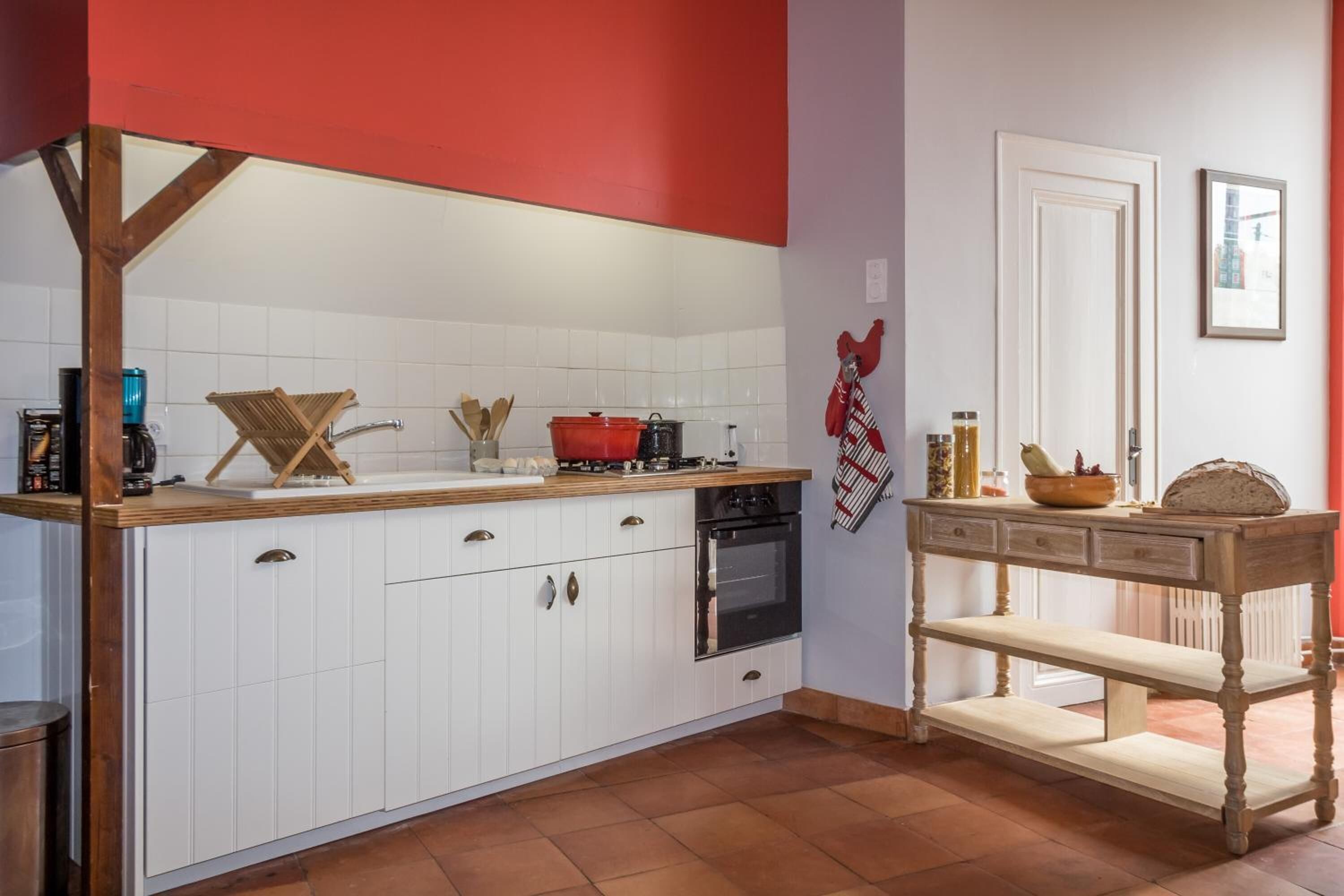 A kitchen with white cabinets, a red accent wall, a wooden table, and a stove.