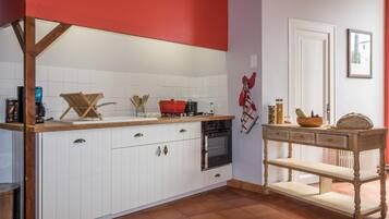 A kitchen with white cabinets, a red accent wall, a wooden table, and a stove.