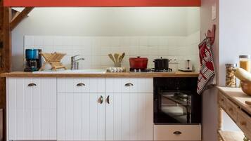 A kitchen with white cabinets, a coffee maker, a red pot, and a wooden chair.