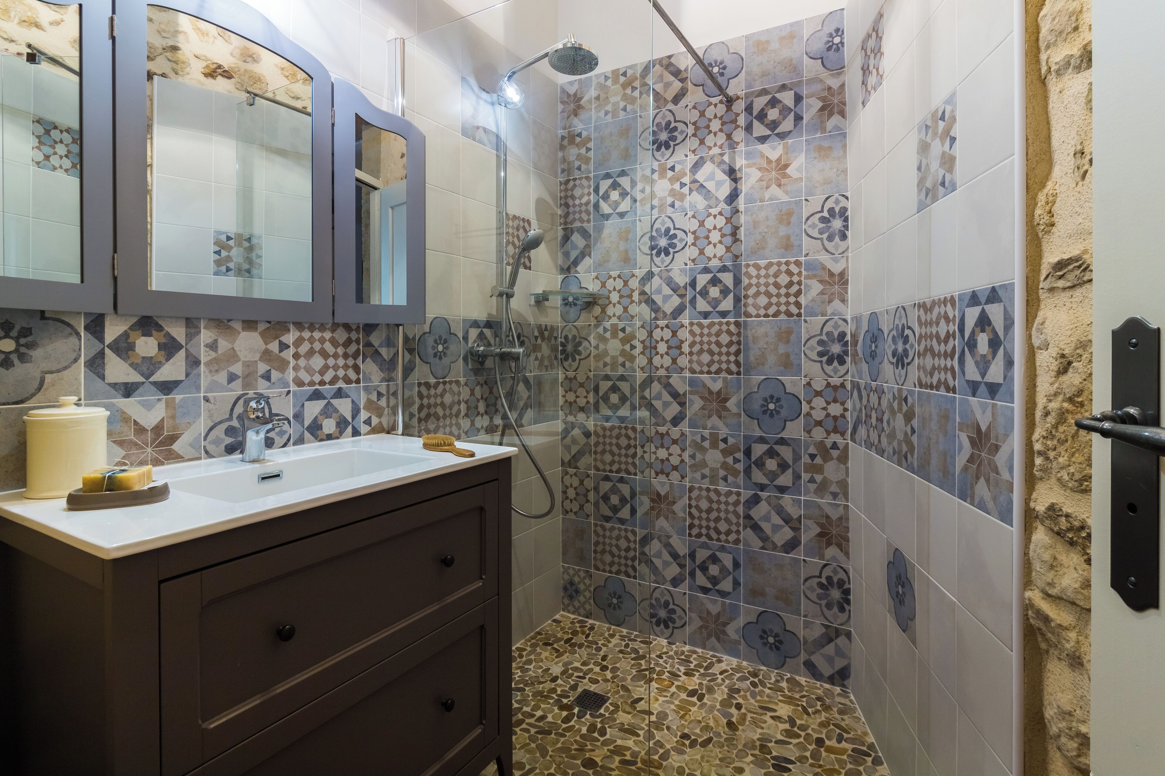 A bathroom with a shower, a sink with a mirror, and patterned tiles.