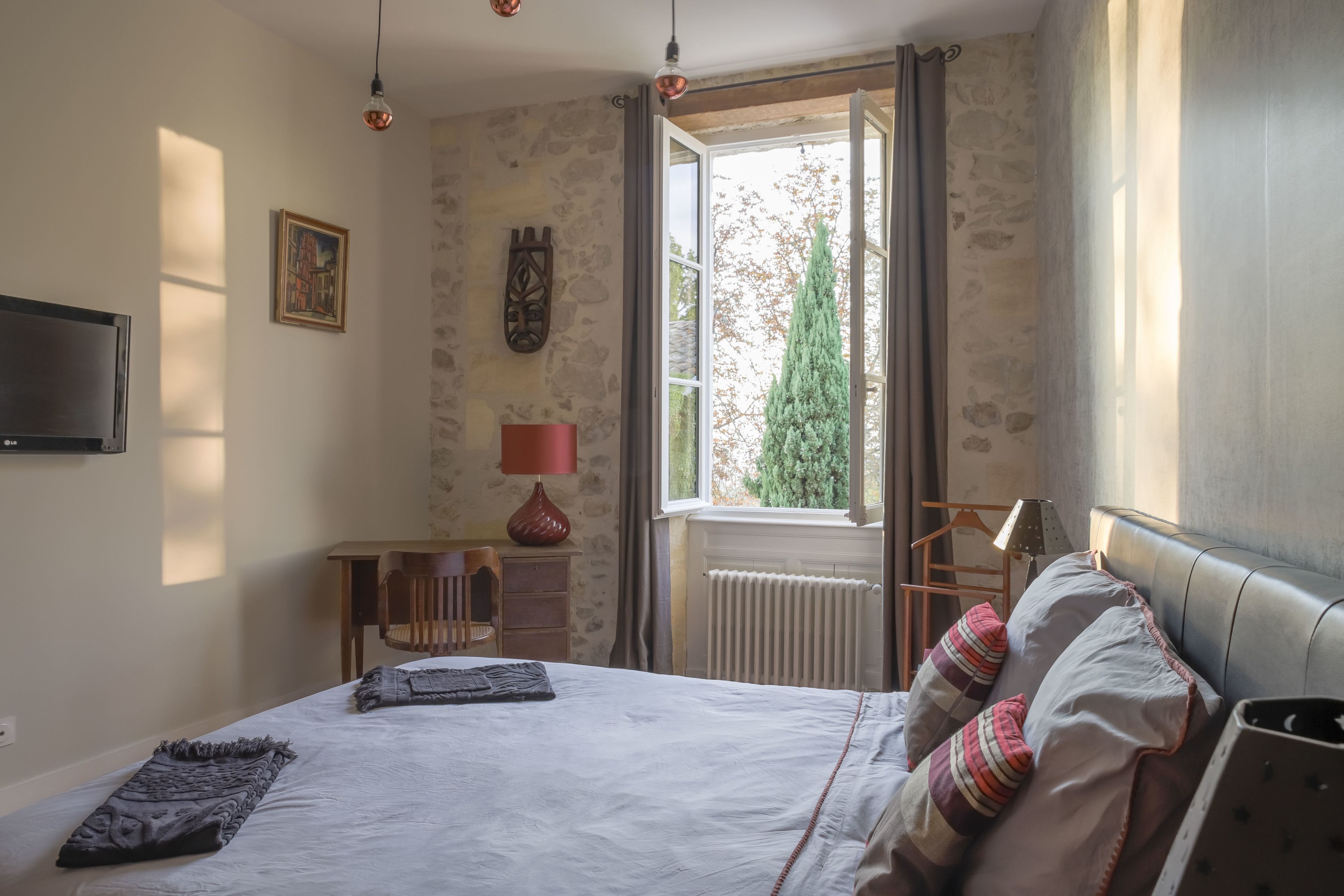 A bedroom with a bed, a window with curtains, a radiator, a TV, and a lamp.