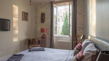 A bedroom with a bed, a window with curtains, a radiator, a TV, and a lamp.