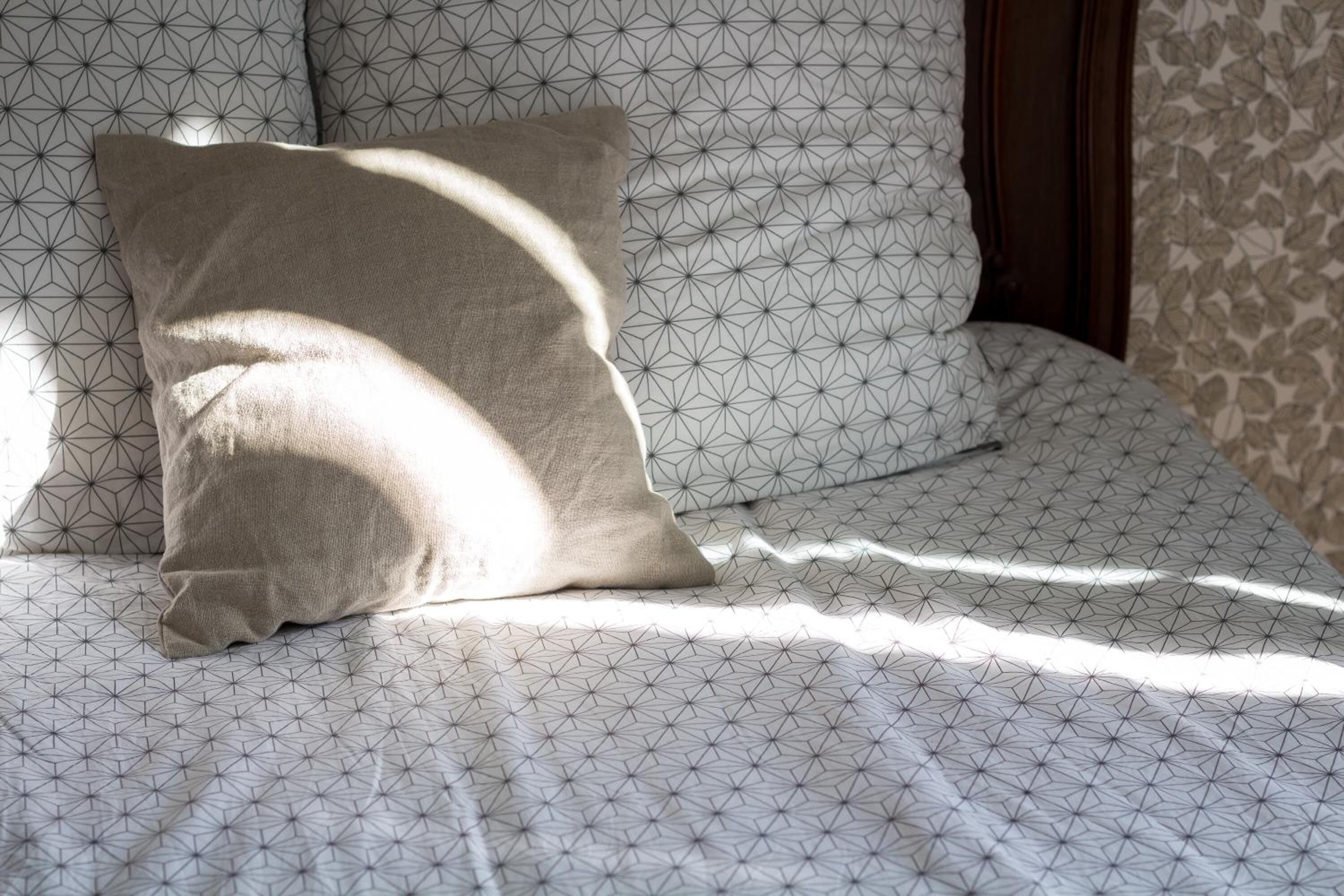 Una cama con una colcha y almohadas de estampado geométrico, un cabecero de madera y un papel tapiz estampado.