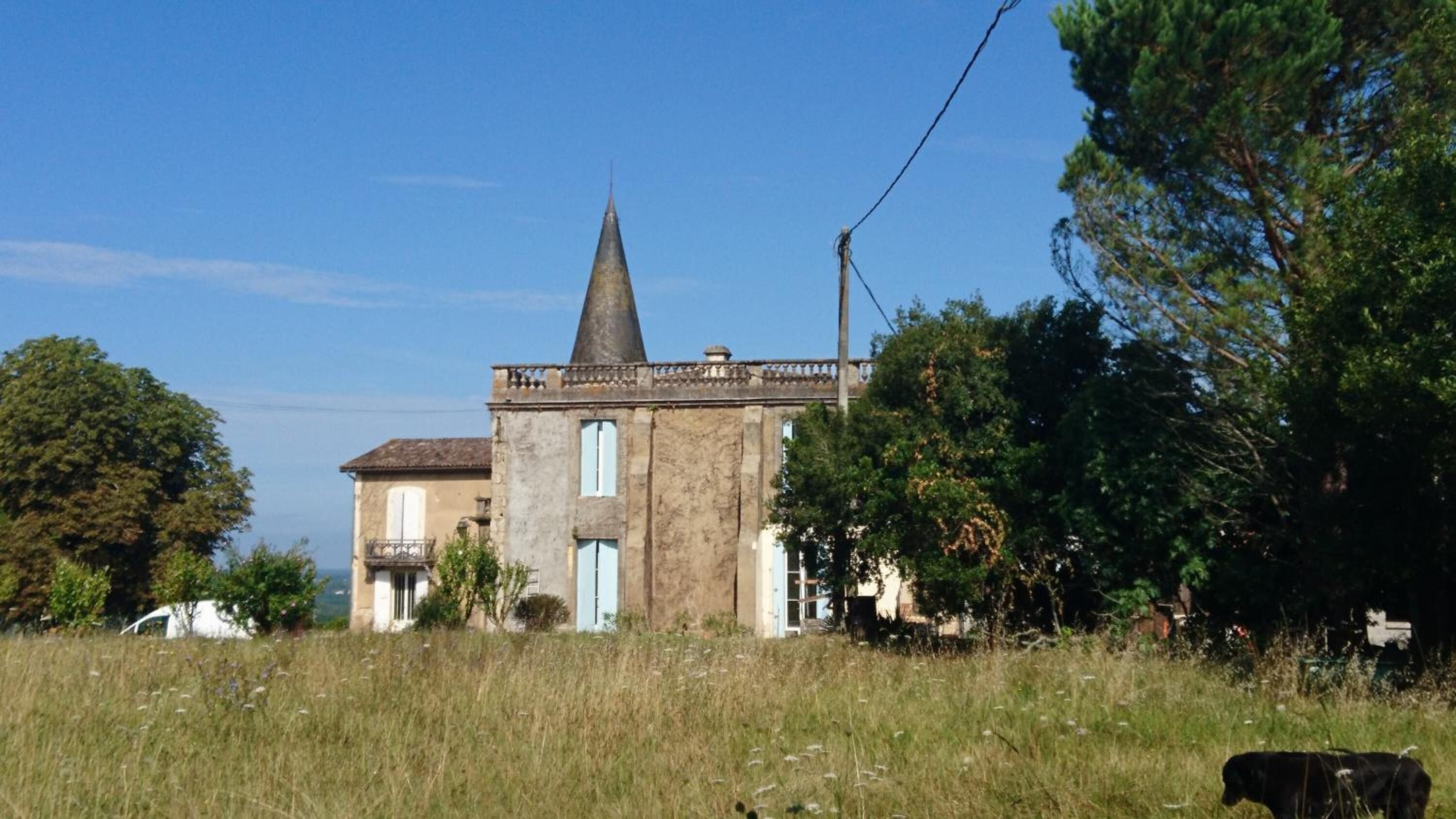 A historic building with a prominent tower, surrounded by a grassy field and trees.