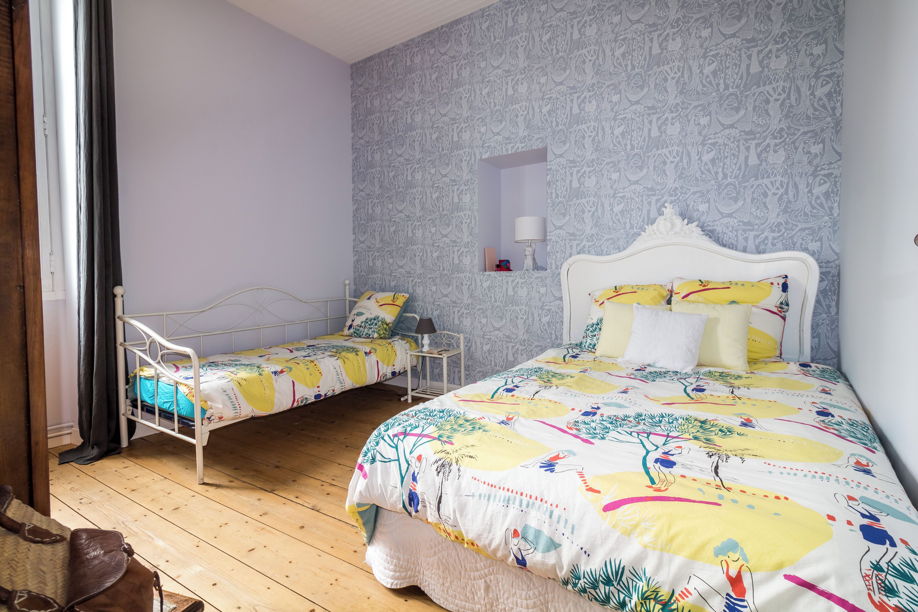 Een slaapkamer met twee bedden, een houten vloer en behang met een patroon.