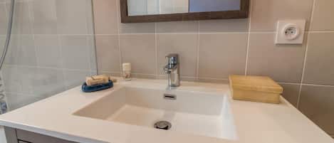 Un baño con un lavamanos blanco, un espejo y un perchero para toallas.