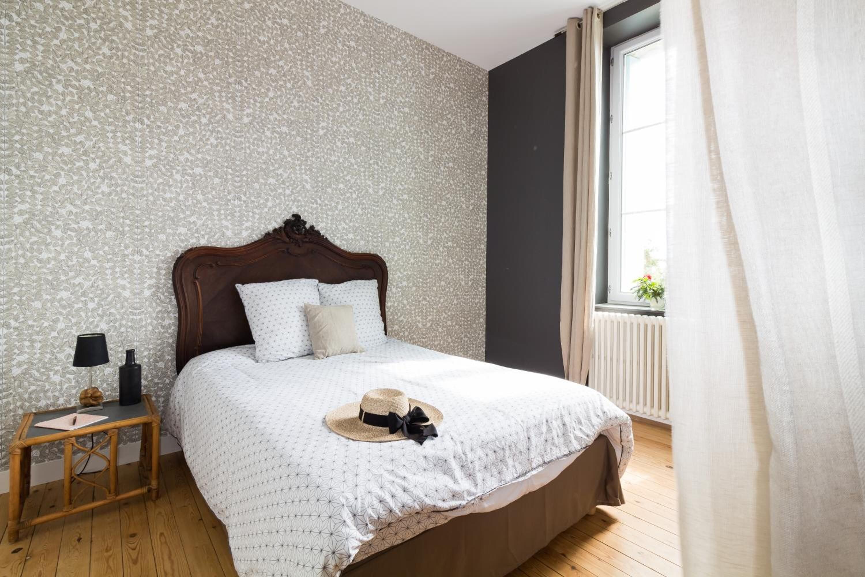 Un lit bien fait, avec une couvre-lit à motifs, une tête de lit en bois et une table de chevet sur laquelle se trouvent une lampe et une bouteille.