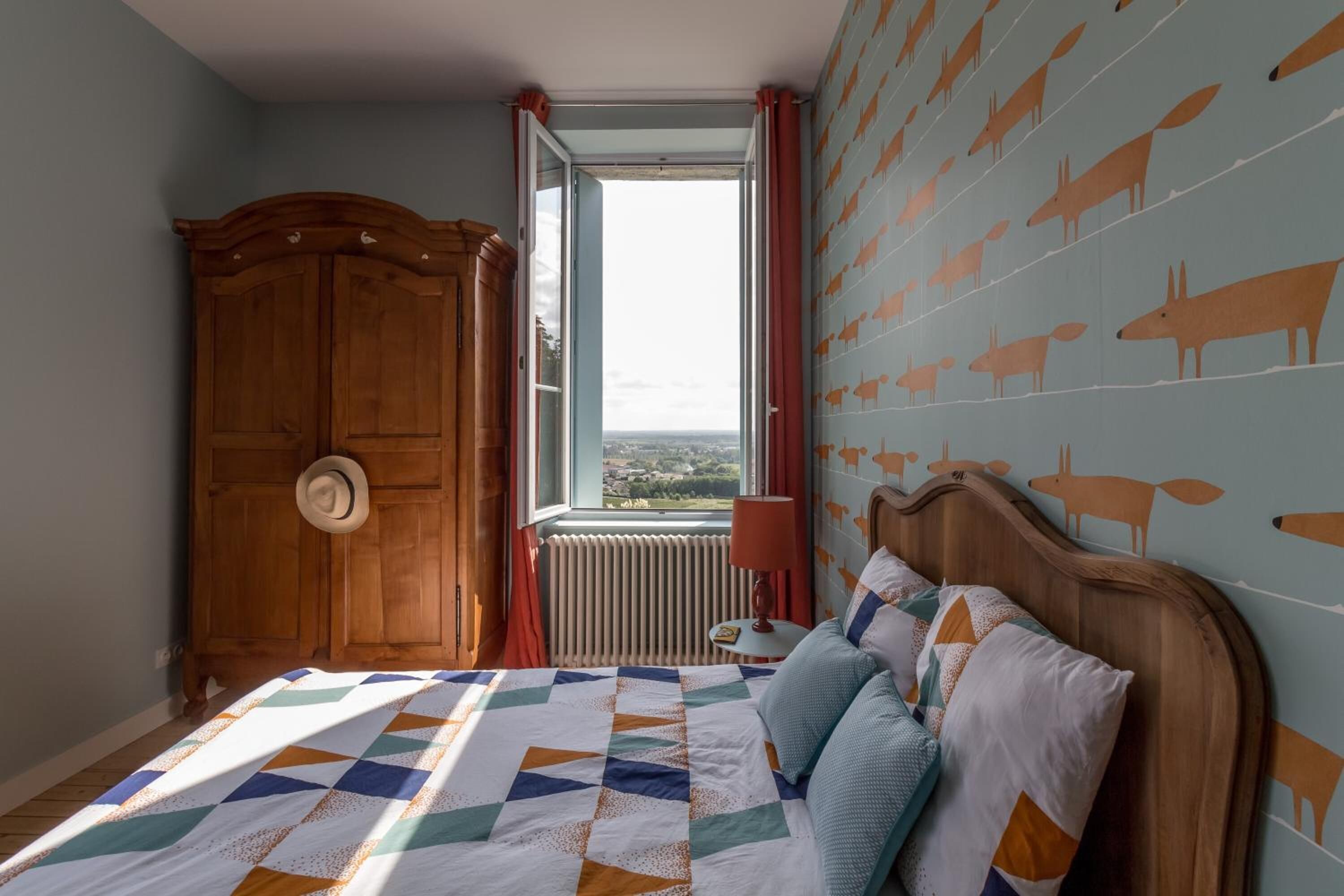 Un dormitorio con una cama grande, un armario de madera, un ventanal con vistas y una pared decorada con motivos de animales.
