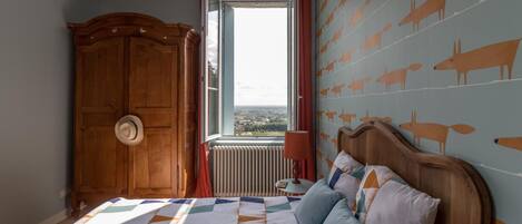 Un dormitorio con una cama grande, un armario de madera, un ventanal con vistas y una pared decorada con motivos de animales.