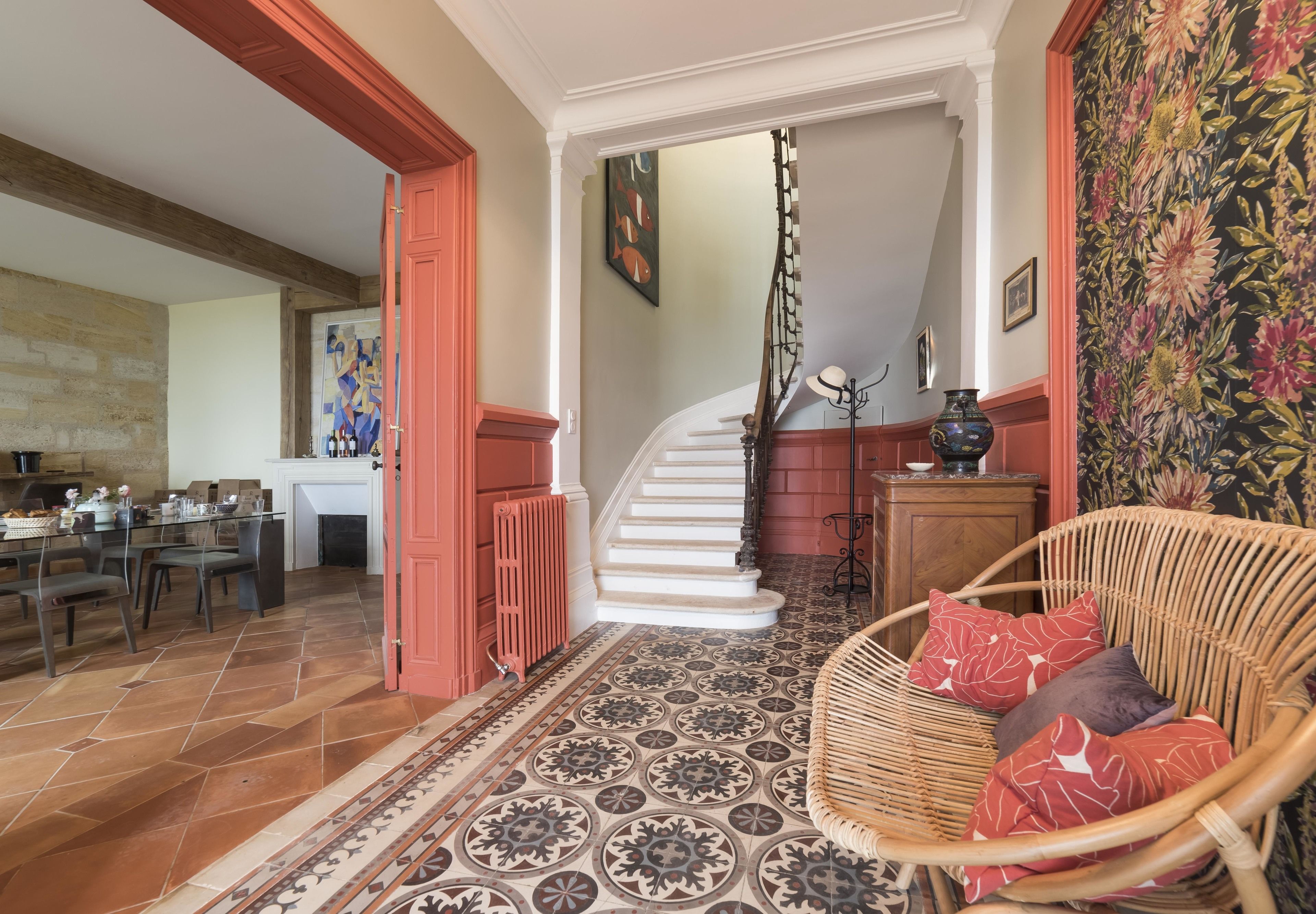 A spacious living area with a dining table, a wicker chair, a patterned rug, and a staircase leading to another level.