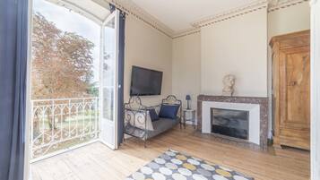 Une pièce comprenant un canapé, une cheminée, un téléviseur et un balcon donnant sur la forêt.