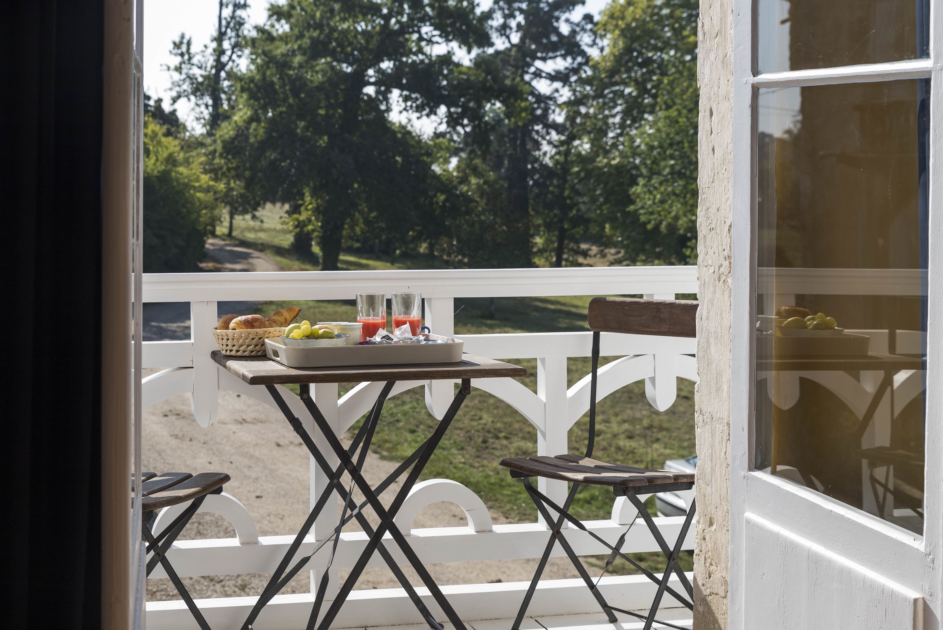 A balcony with a table set for breakfast, overlooking a forested area.