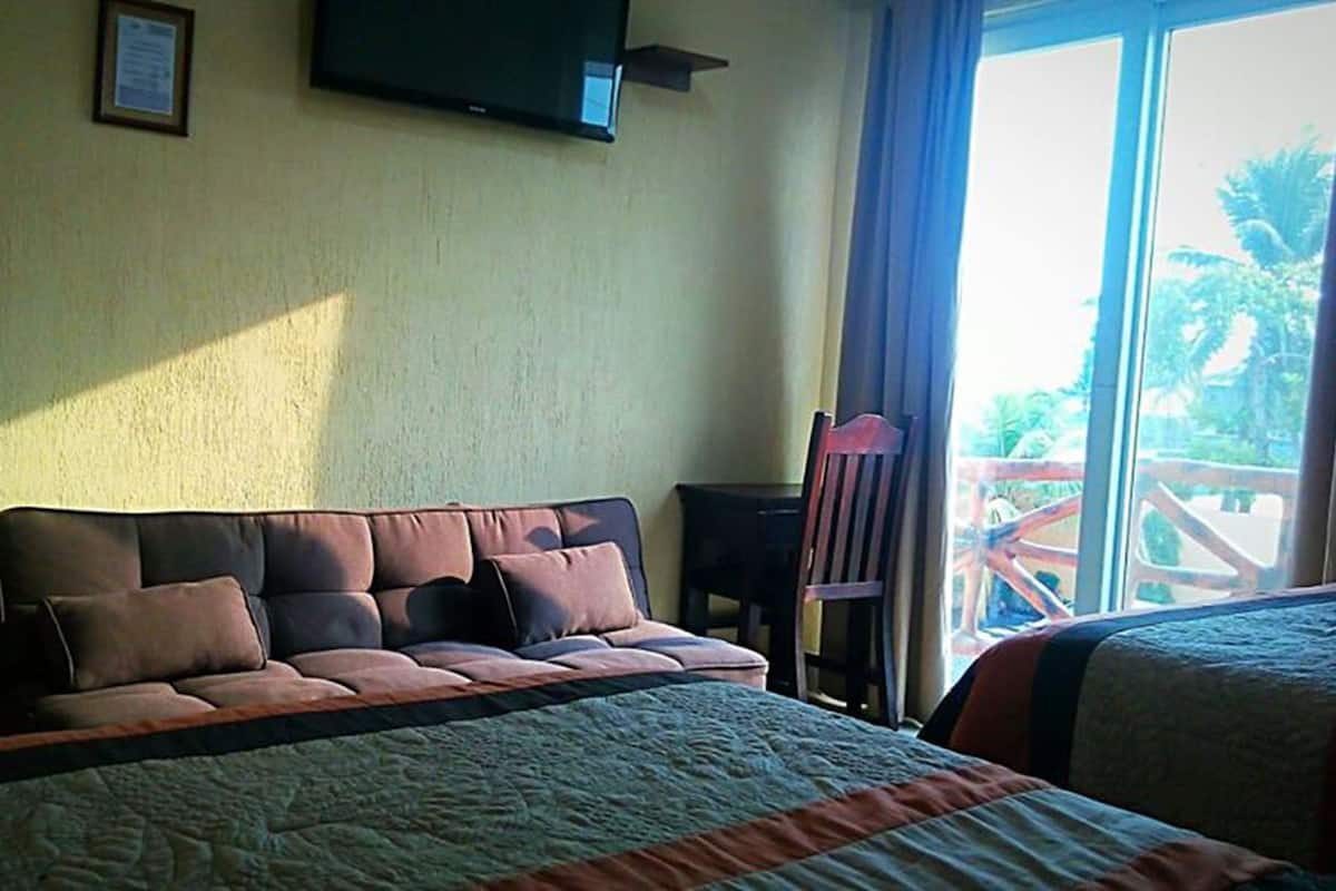 A hotel room with a bed, a sofa, a television mounted on the wall, and a view of the outdoors through a window.