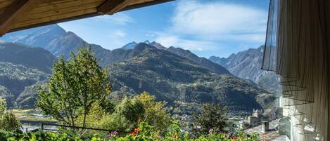 Vista desde un balcón de madera con paisaje montañoso, que incluye un pueblo y una iglesia.
