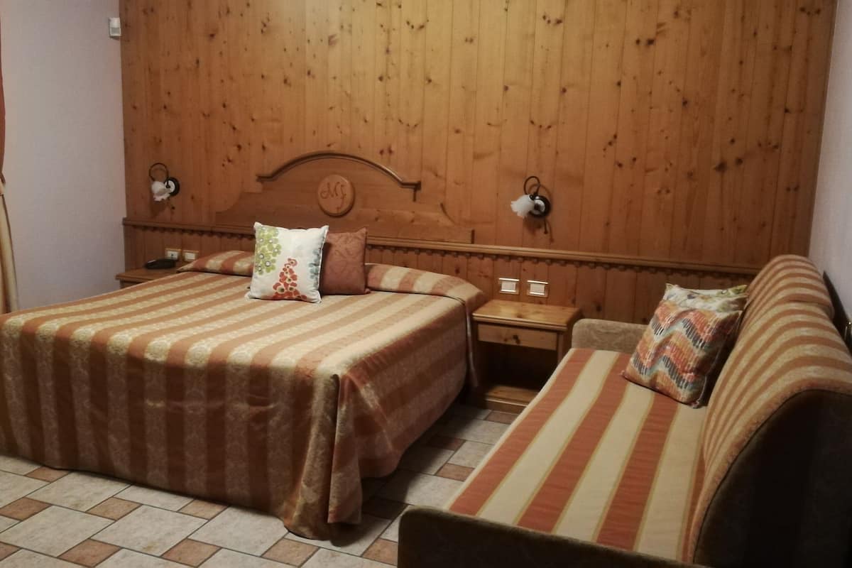 Una habitación de hotel con cabecera de madera, dos camas con ropa de cama a rayas, una mesita de noche y una mesita auxiliar.