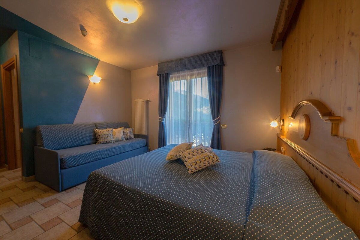 A bedroom with a bed, a sofa, a wooden headboard, and a window with curtains.