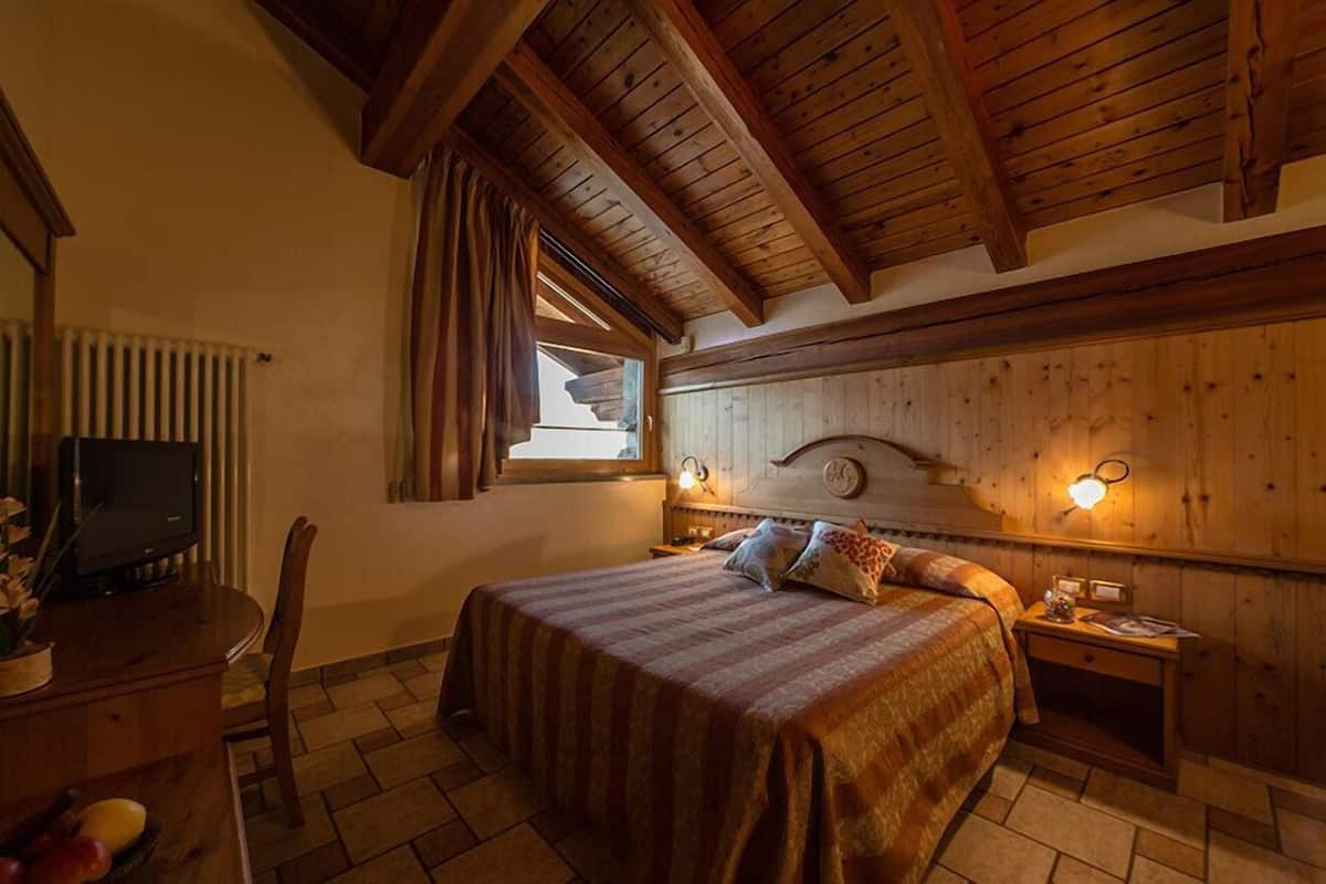 Un dormitorio con cama, cabecera de madera, lámparas de noche, un escritorio con televisor y una ventana con cortinas.