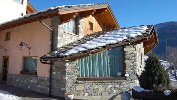 Ein Steinhaus mit geneigtem Schnee bedeckten Dach, großen Fenstern und einem hölzernen Balkon.