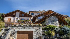 Un bâtiment de style chalet, doté d’une façade en pierre, de balcons en bois et d’un escalier en pierre menant à l’entrée.