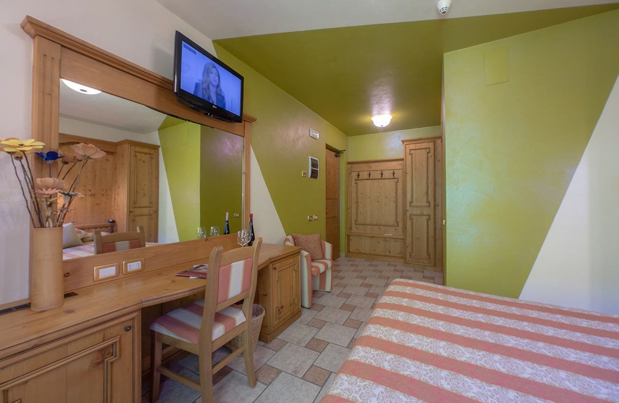 A bedroom with a bed, a wooden desk, a chair, a television, and a wardrobe.