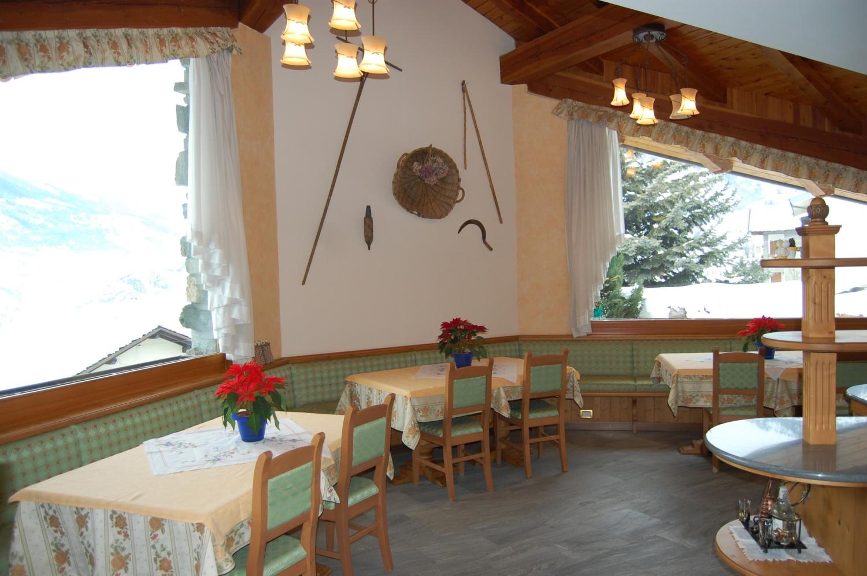 A dining area with wooden tables and chairs, a decorative wall hanging, and a view of the outdoors.