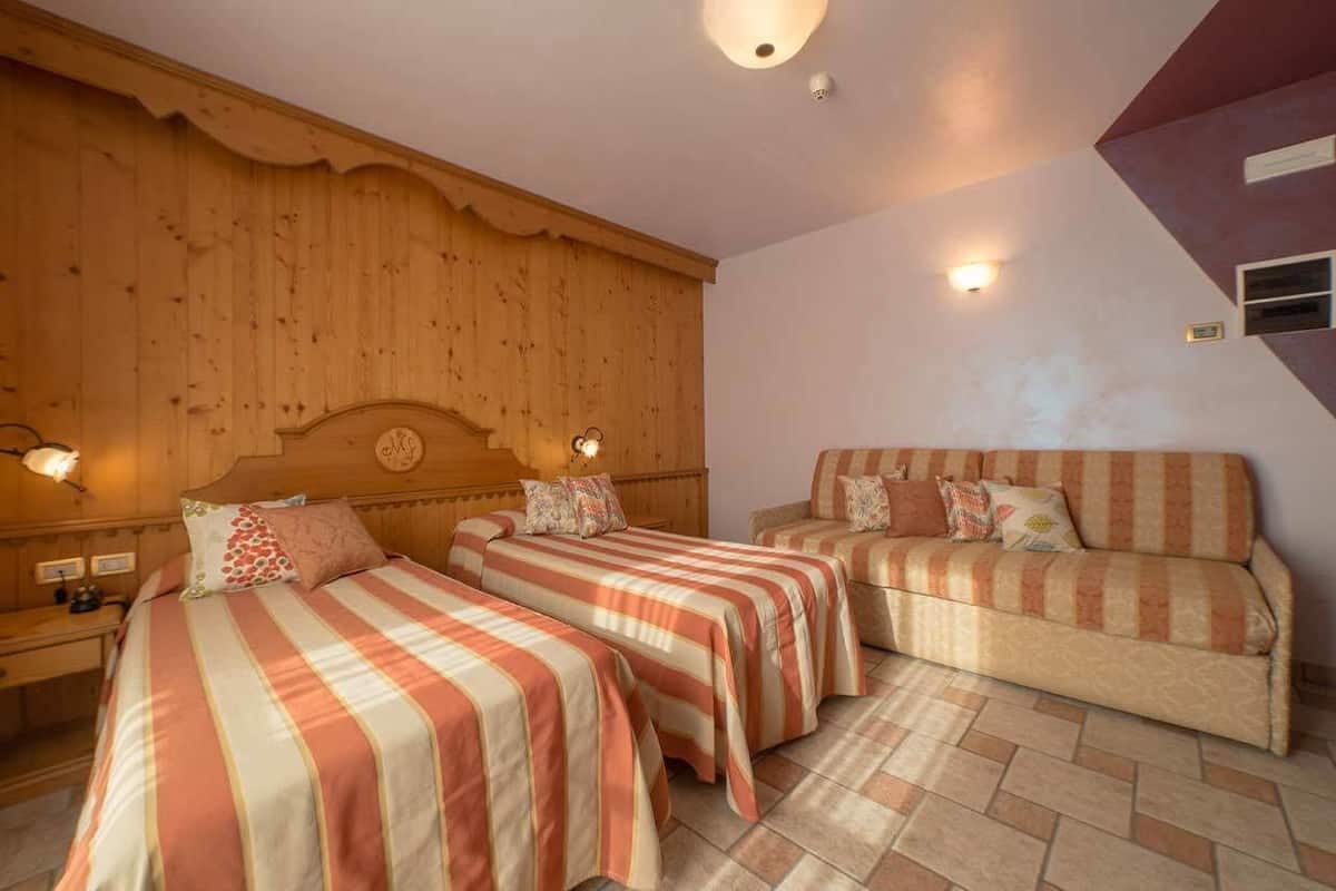 Una habitación con dos camas, un sofá, paneles de madera y luces fijadas a la pared.