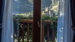 Une vue depuis un balcon doté d’une balustrade en bois, donnant sur un paysage montagneux parsemé de bâtiments et de verdure.
