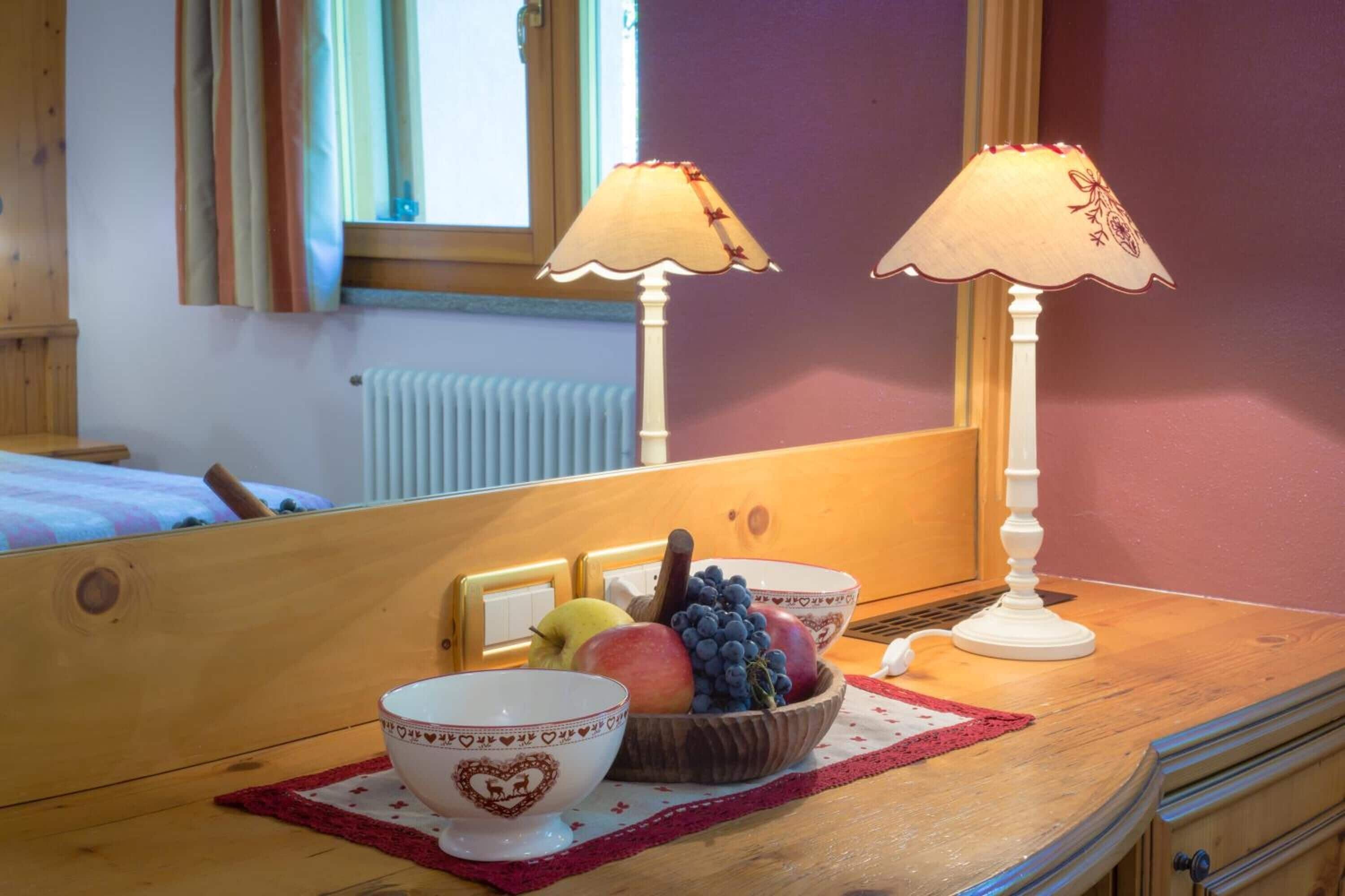 A wooden table with two white lamps, a bowl of fruit, and a heart-shaped bowl.