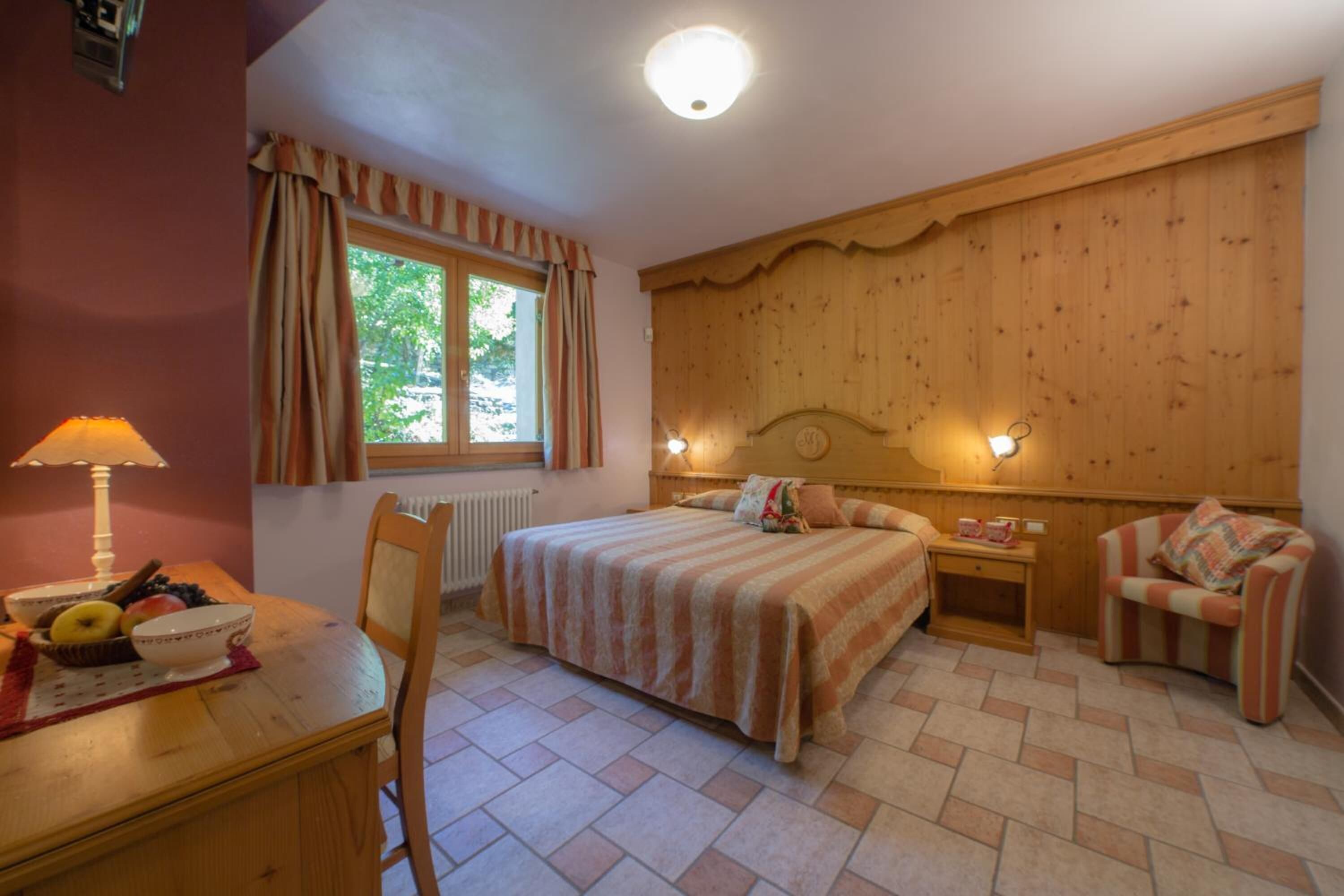 Un dormitorio con una cama, dos mesitas de noche, una silla, una lámpara y una ventana con cortinas.
