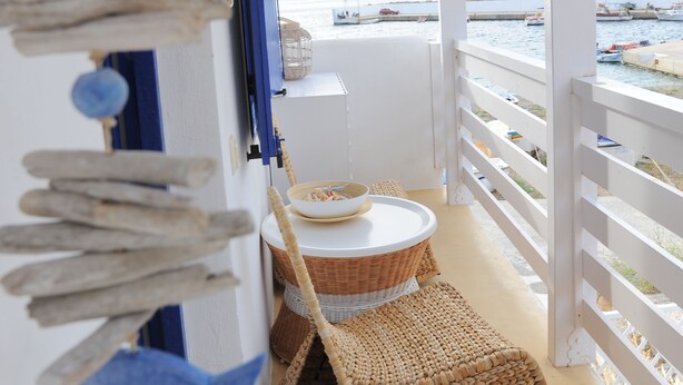 Een balkon met uitzicht op zee, een rieten stoel en een geweven mat.