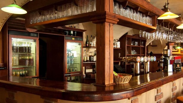 A bar area with wooden shelves, hanging glasses, and a refrigerator stocked with bottles. - Hotel Caffe Silesia (Frydek-Mistek)