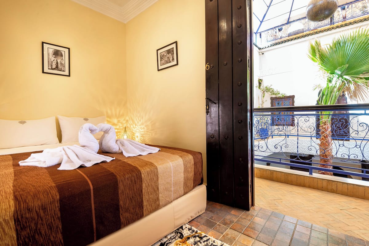 Une chambre d’hôtel avec un lit, deux tableaux encadrés au mur, un balcon avec vue et une porte.