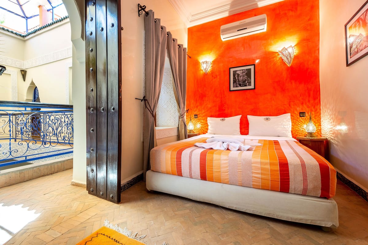 Une chambre d’hôtel avec un lit, une fenêtre avec des rideaux, un appareil de climatisation et une vue sur un balcon.