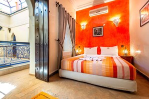 A hotel room with a bed, a window with curtains, an air conditioning unit, and a view of a balcony. - Riad Kamal (Marrakech)