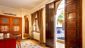 A hotel room with a wooden door, a glass table, a chair, a patterned rug, and a window with curtains. - Riad Kamal (Marrakech)