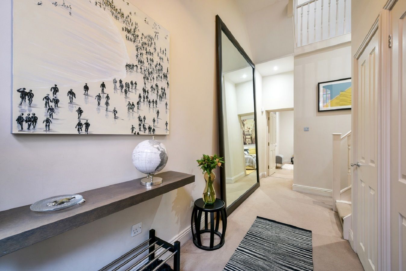 A hallway with a large mirror, a globe, and a painting of people walking.