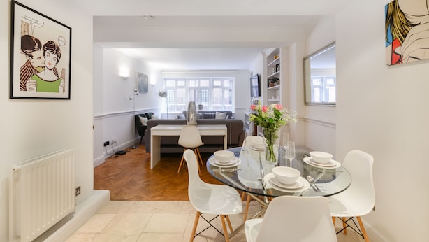 A modern dining area with a glass table, white chairs, and a vase of flowers. - Cavendish - By Sojourn (London)