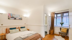 A modern bedroom with a large bed, a bedside table, a chair, and a window with curtains. - Cavendish - By Sojourn (London)