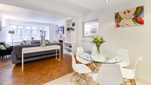 A modern living room with a sofa, a glass dining table, and white chairs. - Cavendish - By Sojourn (London)