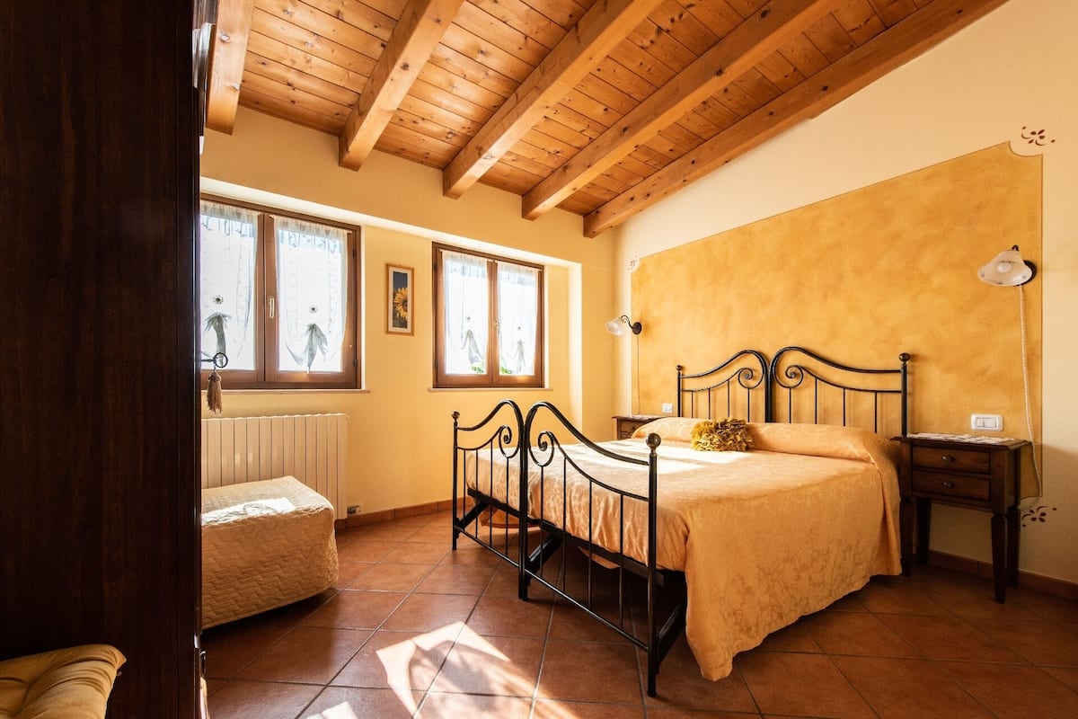 A bedroom with a bed, a nightstand, a window, and a radiator.