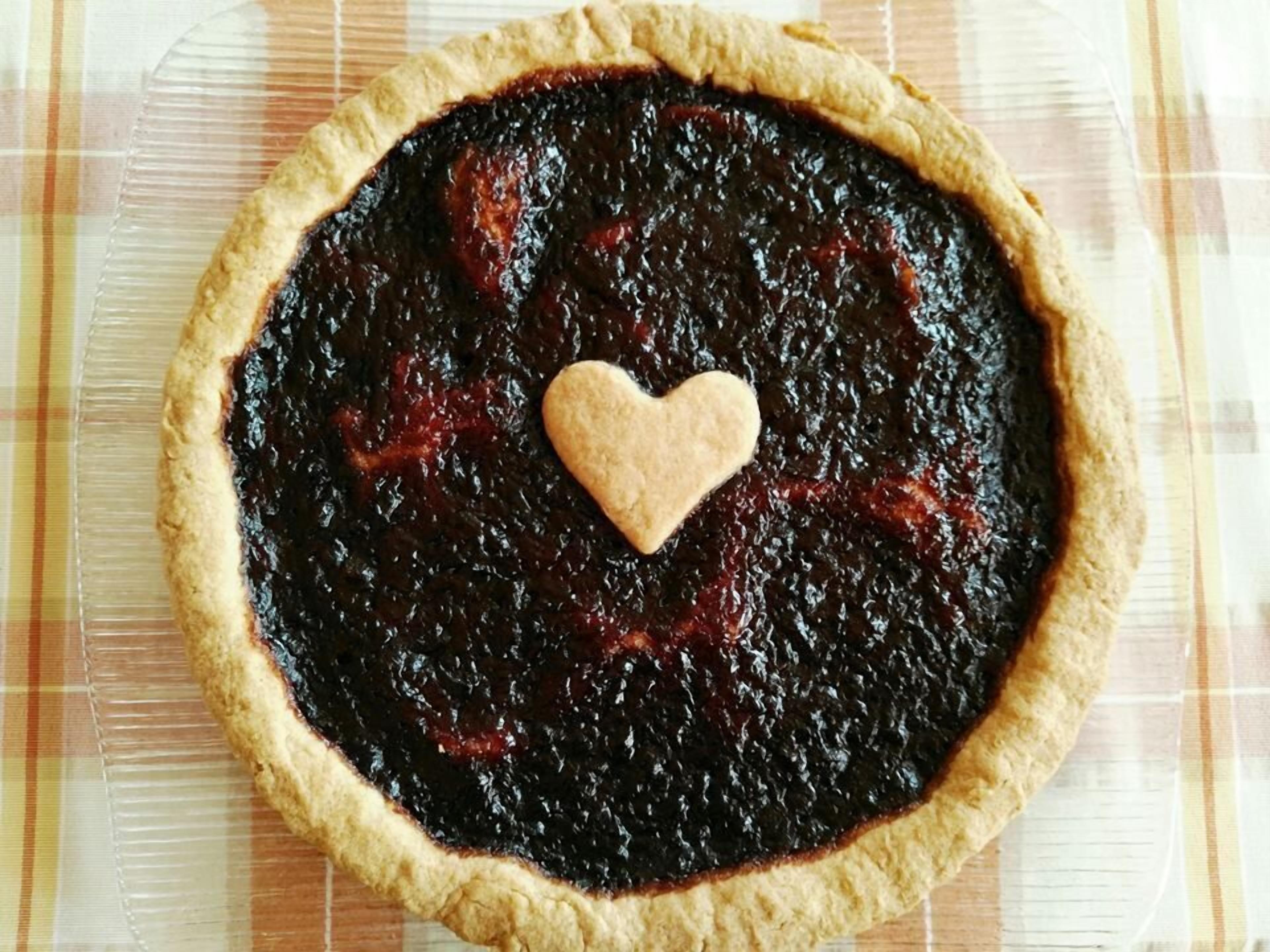 Une tarte surmontée d’un biscuit en forme de cœur, posée sur une nappe à carreaux.